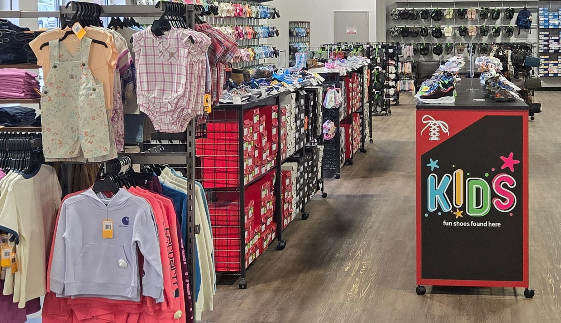 Kids clothing and shoes on racks inside a Super Shoes store.