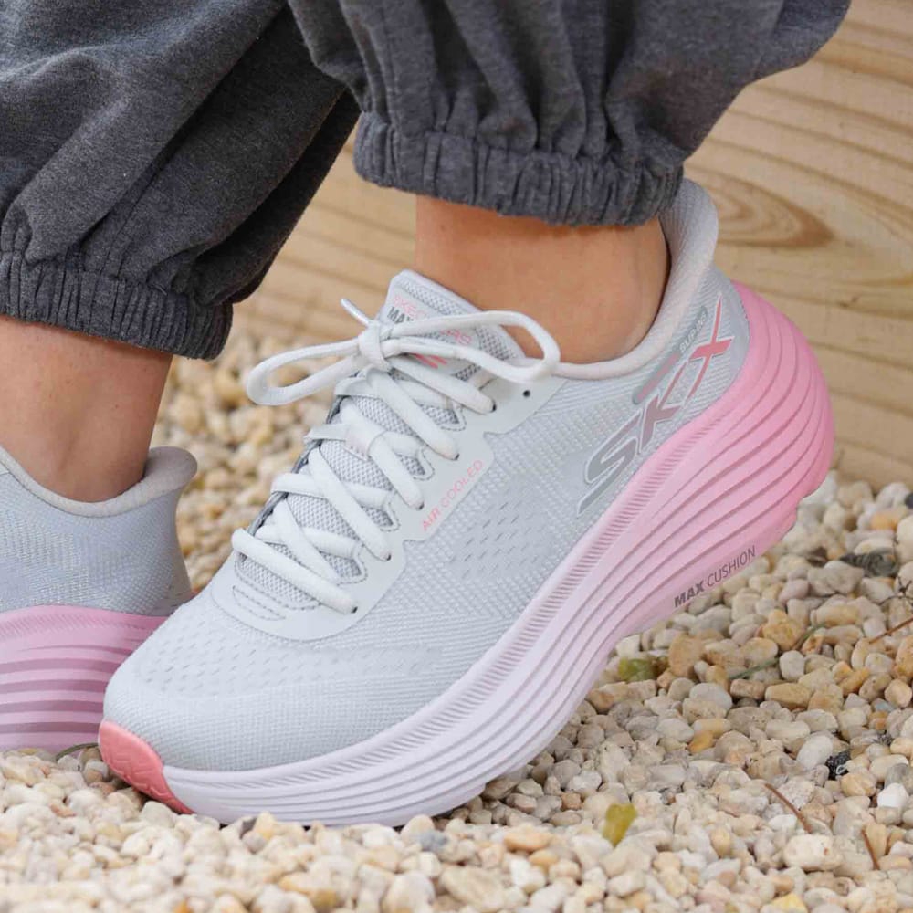 A woman wearing grey and pink Skechers sneakers.